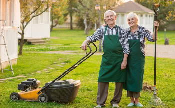 Cuidado del jardín por adultos mayores con cortacésped y herramienta, en un espacio verde y soleado.