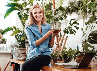 Chica sonriente sosteniendo un regalo envuelto en un entorno con plantas verdes y luz natural